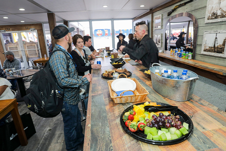 Attendees at a bar with food and beverages on it, talking with the barkeeper.