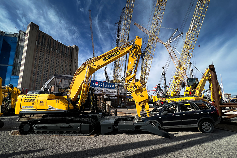 Wide shot of car demolition excavator reaching into a car engine compartment